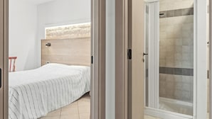Un dormitorio con cama, cabecero de madera y zona de ducha con paredes de azulejos.