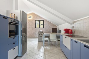 Een moderne keuken met een inbouwoven, een eethoek met een tafel en stoelen, en een rode waterkoker op het aanrecht.