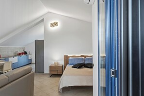 Een moderne slaapkamer met een groot bed, een nachtkastje, een klein tafeltje en een kitchenette op de achtergrond.