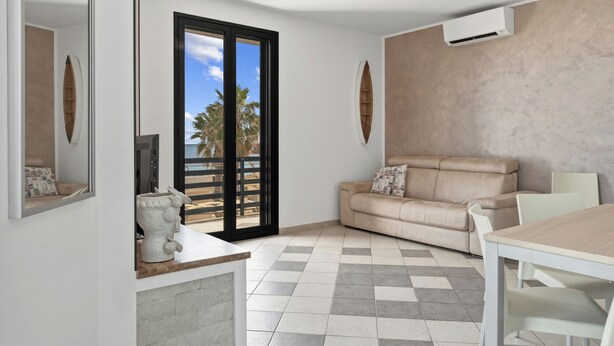 Una sala de estar moderna con un sofá color beige, una mesa de comedor y un ventanal con vista a palmeras.