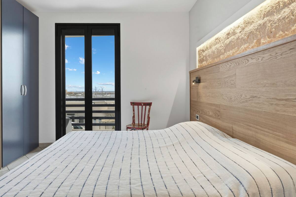 A bedroom with a bed, a wooden headboard, a chair, and a view through a door.