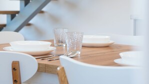 Un comedor con una mesa de madera, sillas blancas y una escalera al fondo.