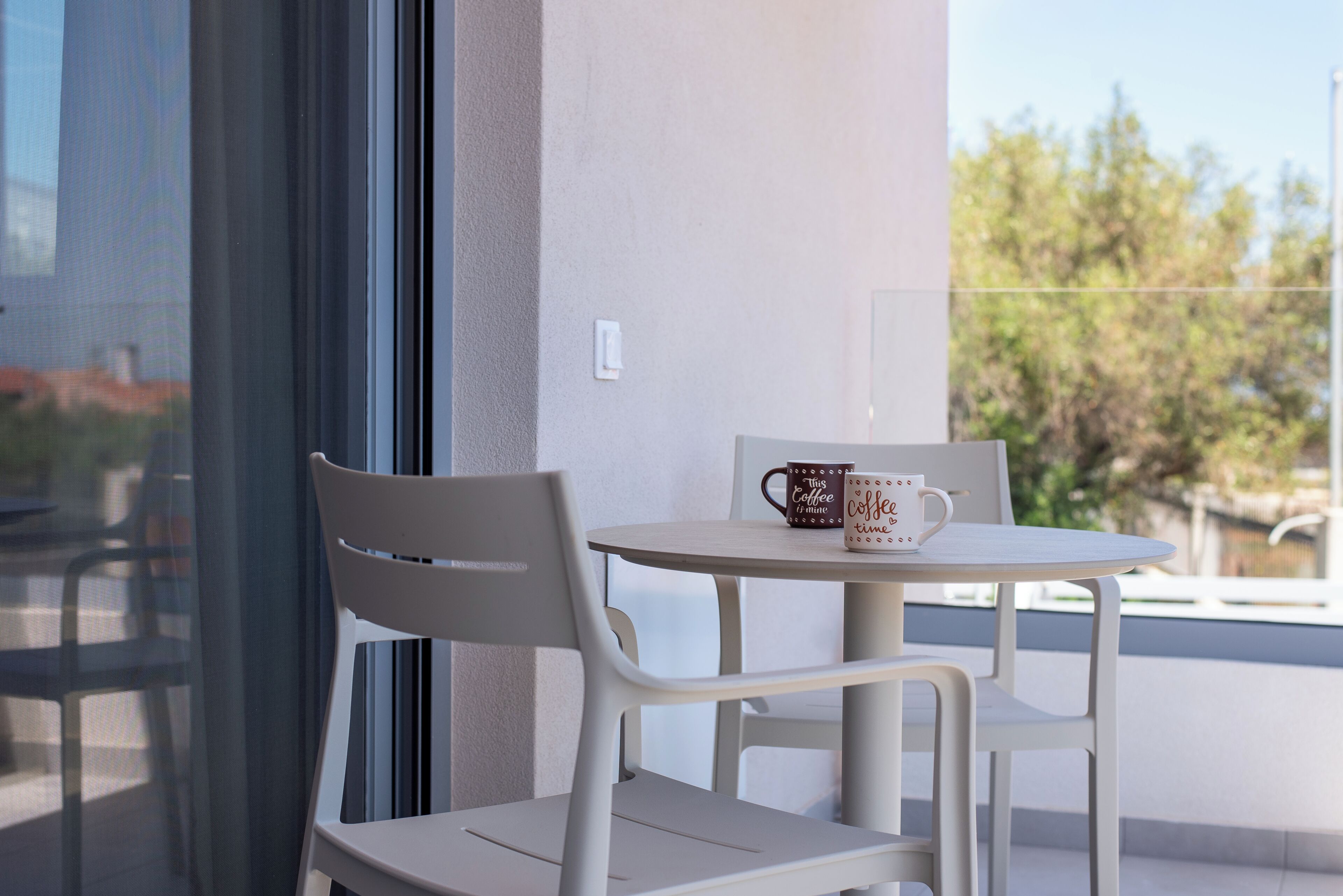 A white table and chairs on a balcony with a coffee mug on the table.