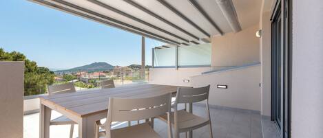 A balcony with a table and chairs, a view of the sea, and a mountain in the distance.