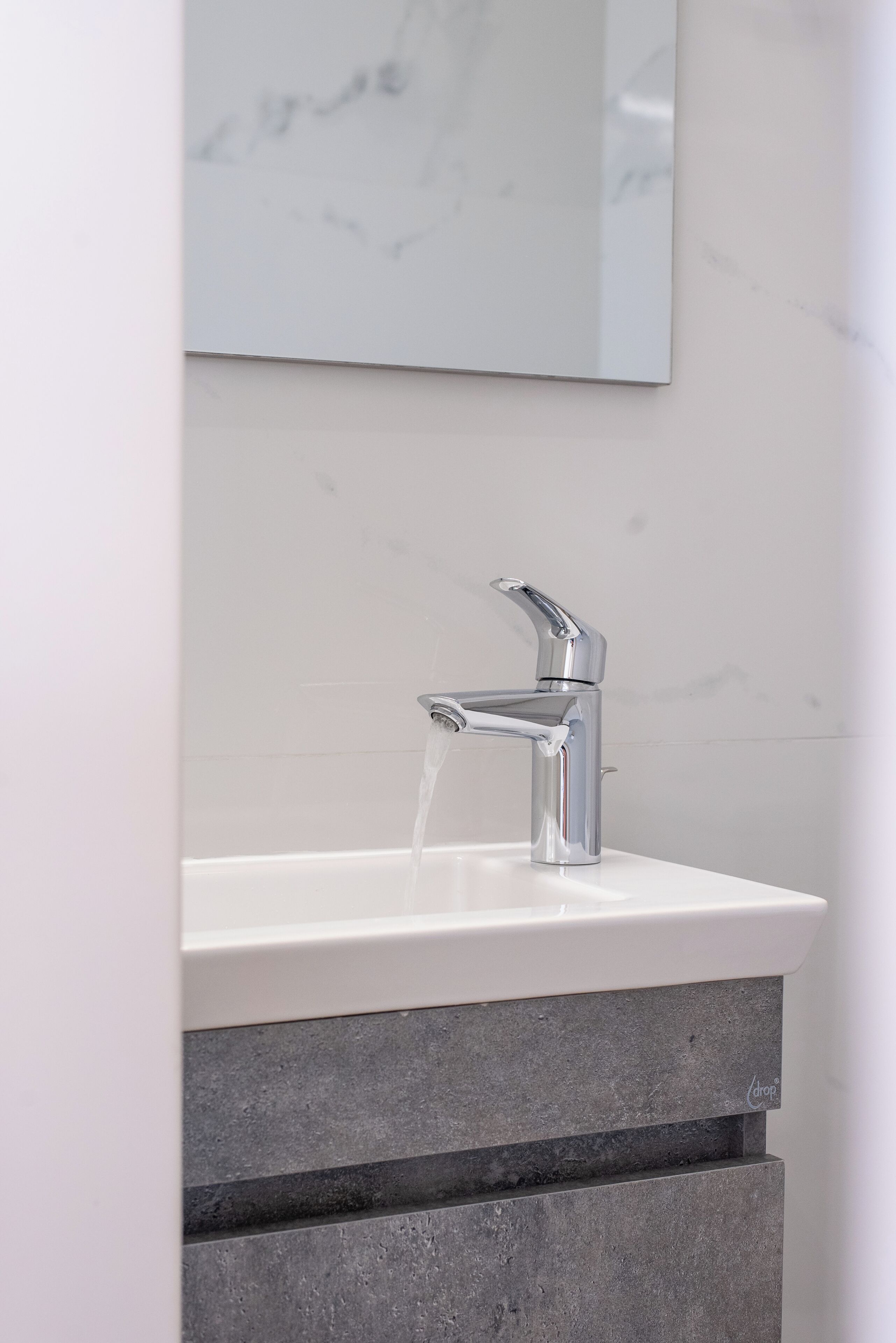 A bathroom with a white sink, chrome faucet, and a marble wall.