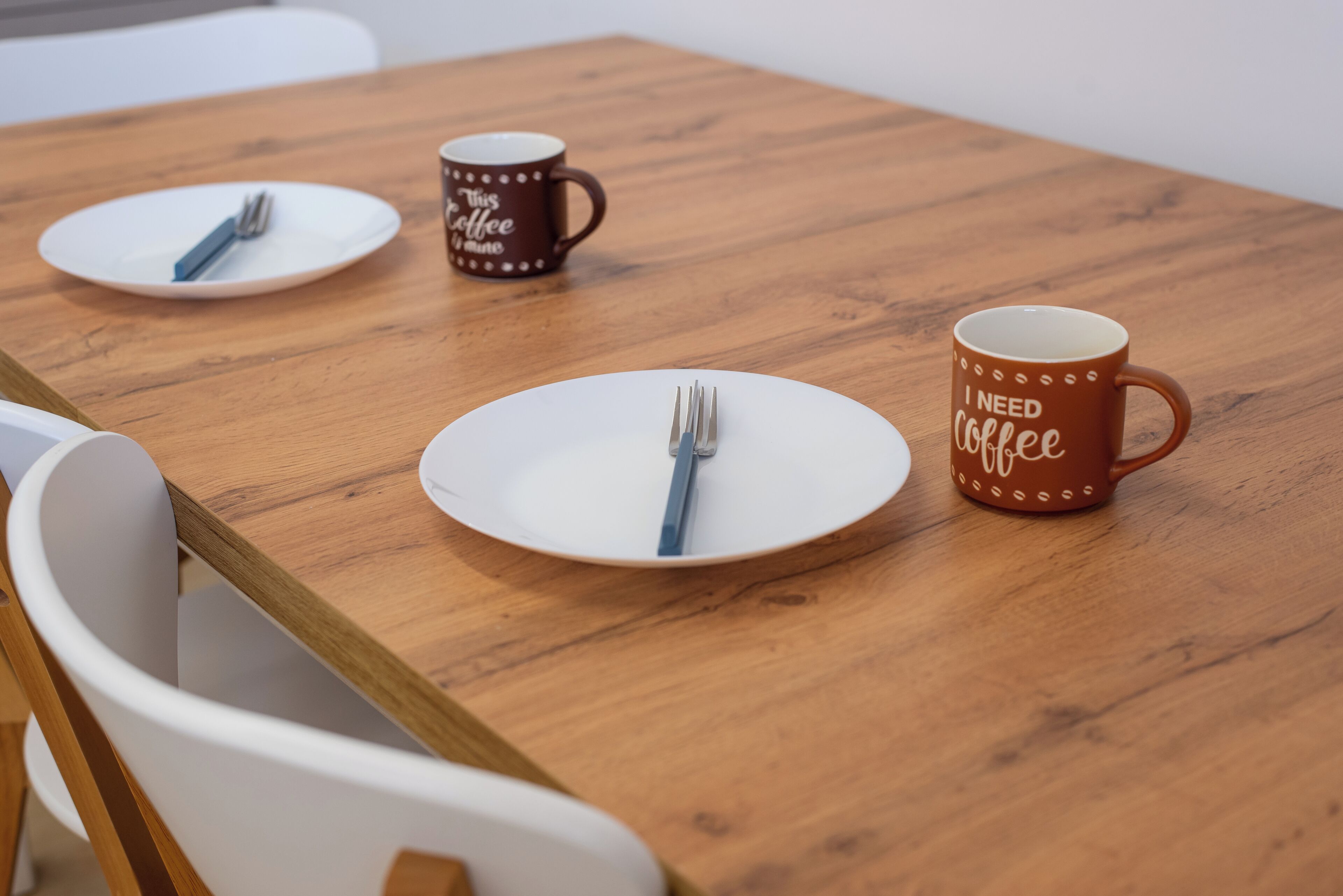 A wooden table with two white plates and two coffee mugs.