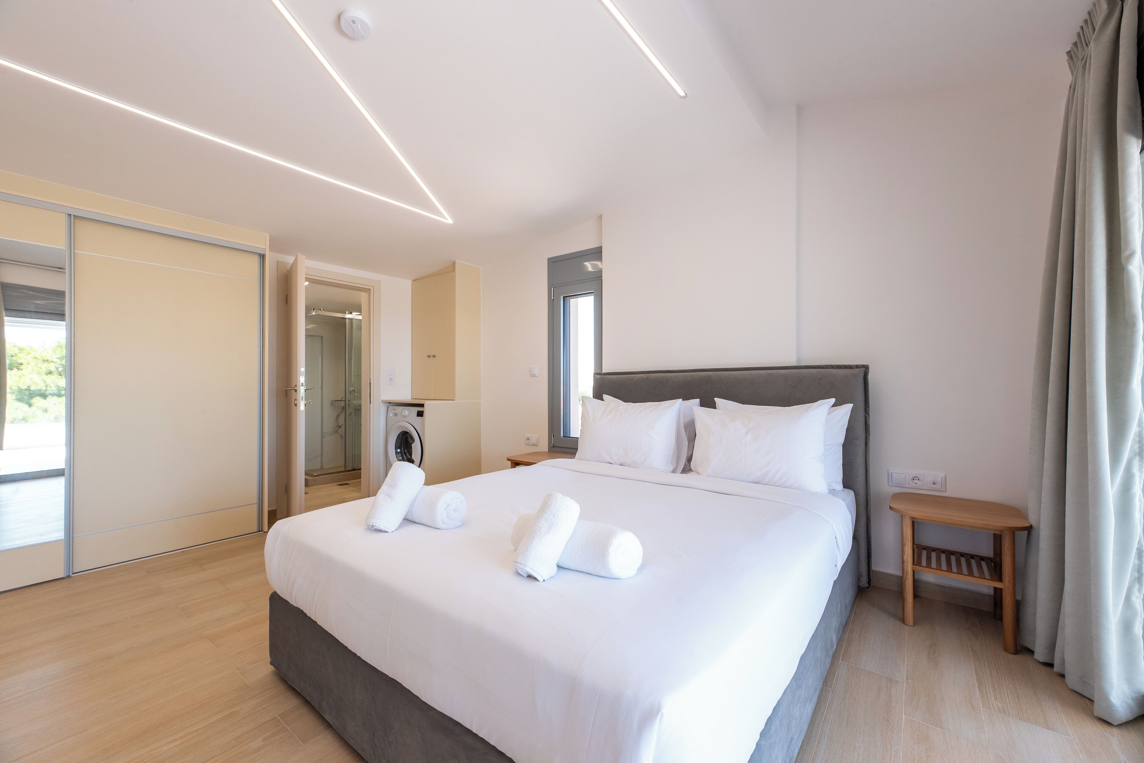A modern hotel room with a large bed, a bedside table, a shower area, and a view of the outdoors.