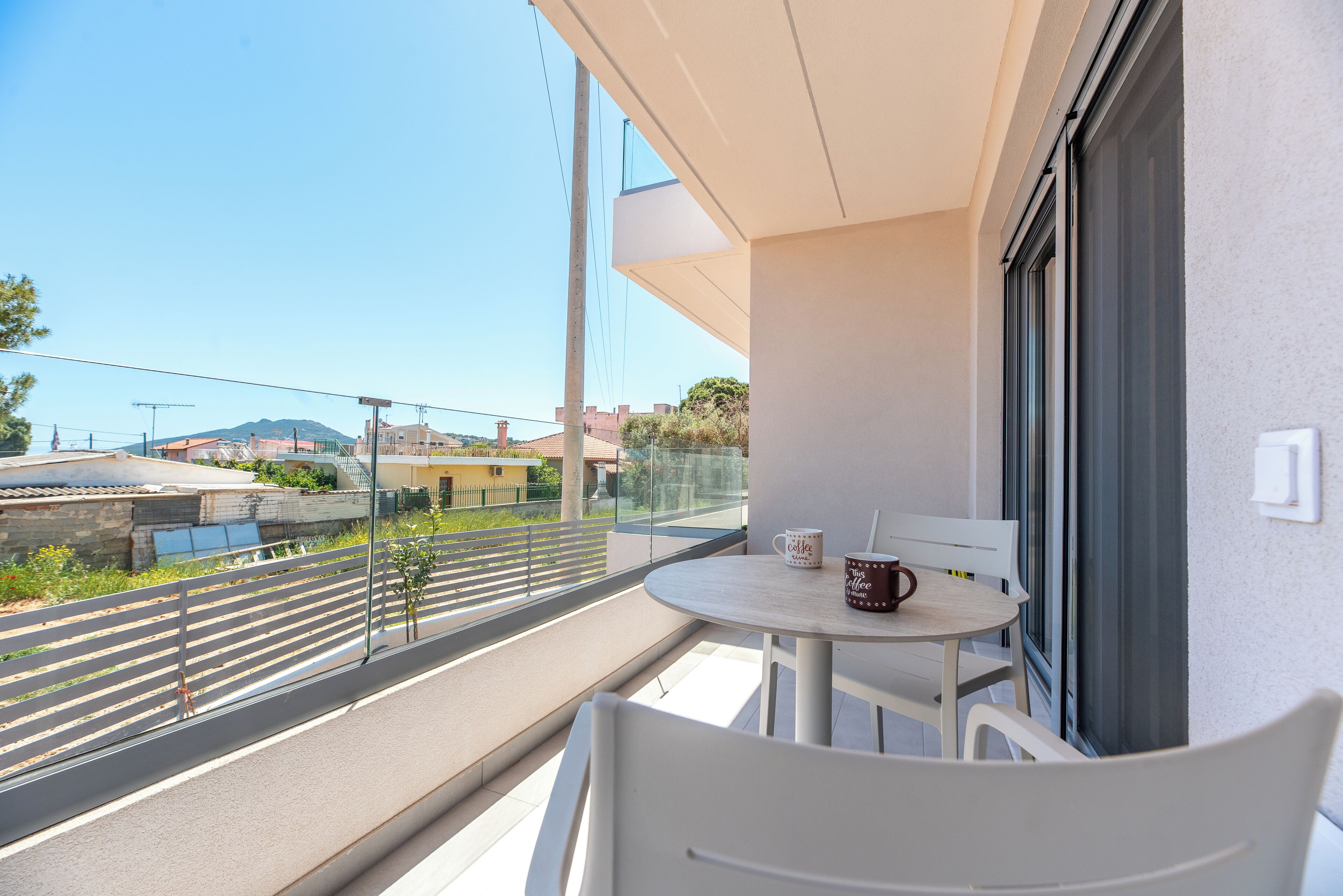 A balcony with a table and chairs, a view of the street, and a building in the background.