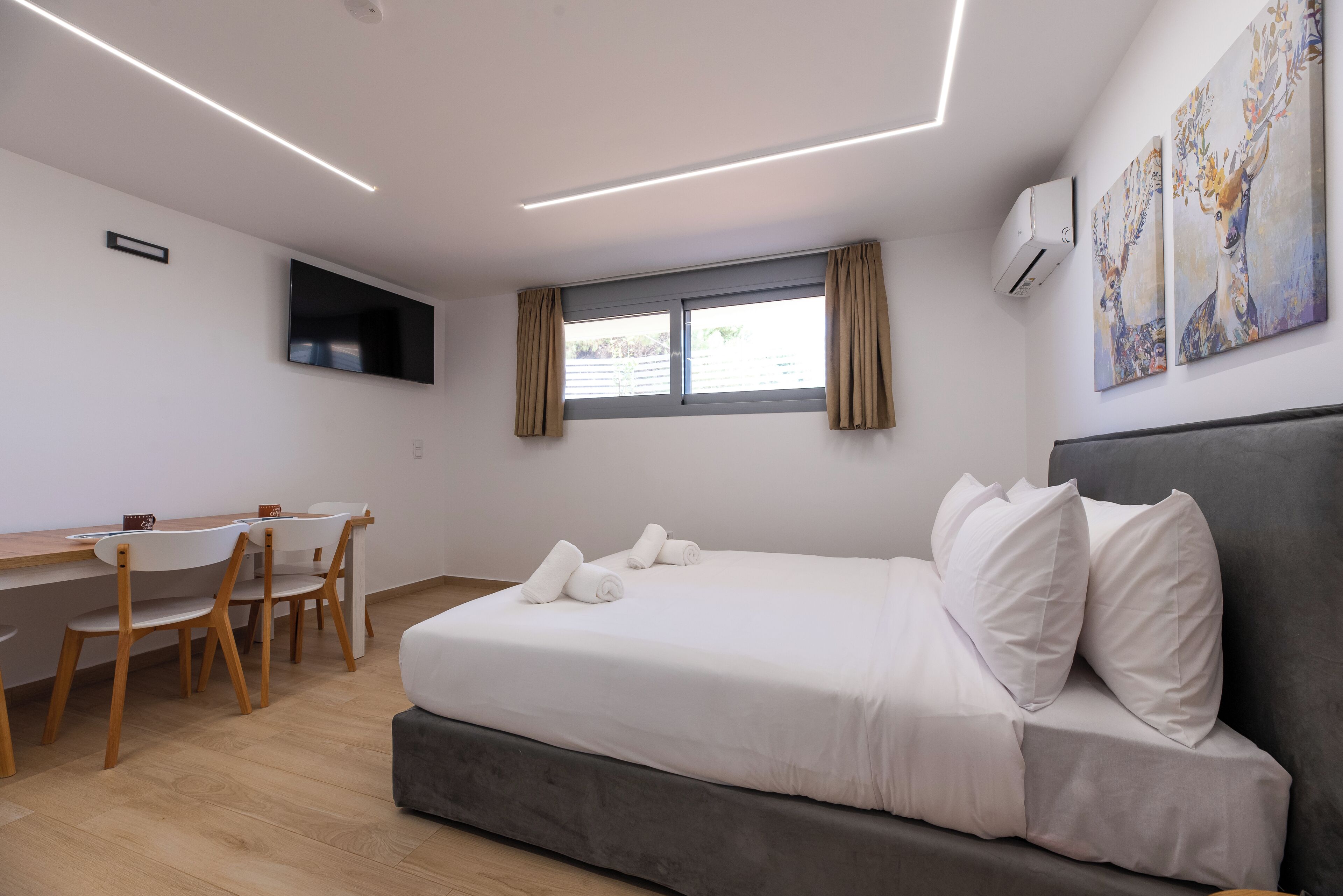 Una habitación de hotel moderna con una cama, un escritorio, sillas, un televisor y obras de arte en la pared.