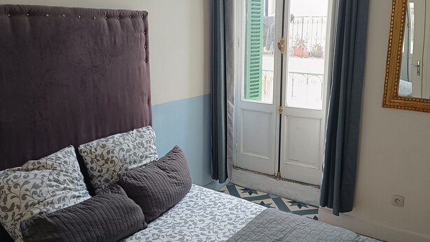 Une chambre à coucher avec un lit, une fenêtre avec des rideaux et un miroir au mur.