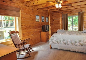 Une pièce de style cabane en bois, comprenant un lit, un fauteuil à bascule, une télévision et un ventilateur de plafond.