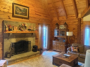 Interior acogedor de una cabaña con chimenea de piedra, paredes de madera, un cuadro colgado y un mueble de madera con puertas de cristal.