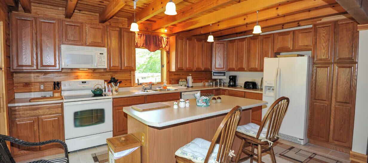 Une cuisine avec des meubles de rangement en bois, un îlot central doté de chaises, une cuisinière et un réfrigérateur.