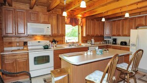 Una cocina con armarios de madera, una isla central con sillas, estufa y refrigerador.
