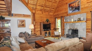 Interior acogedor de una cabaña de madera con chimenea, sofás cómodos, un televisor y techo de madera.