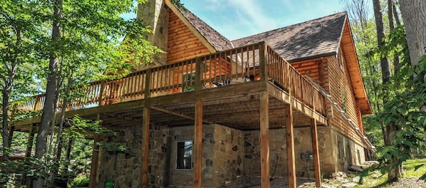 Un chalet rustique doté d’une terrasse en bois et de murs en pierre, entouré d’arbres.