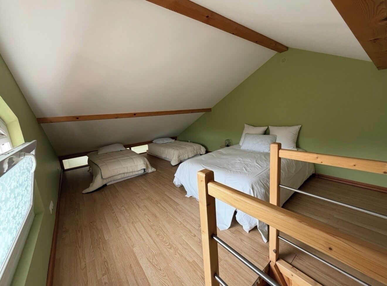 A room with a sloped ceiling, wooden beams, a bunk bed, and a window.