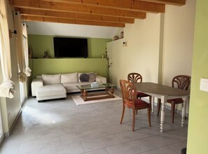 A living room with a sofa, a glass coffee table, wooden chairs, a dining table, and a TV mounted on the wall. - Superb T3 quiet with private parking min Geneva (Vétraz-Monthoux)