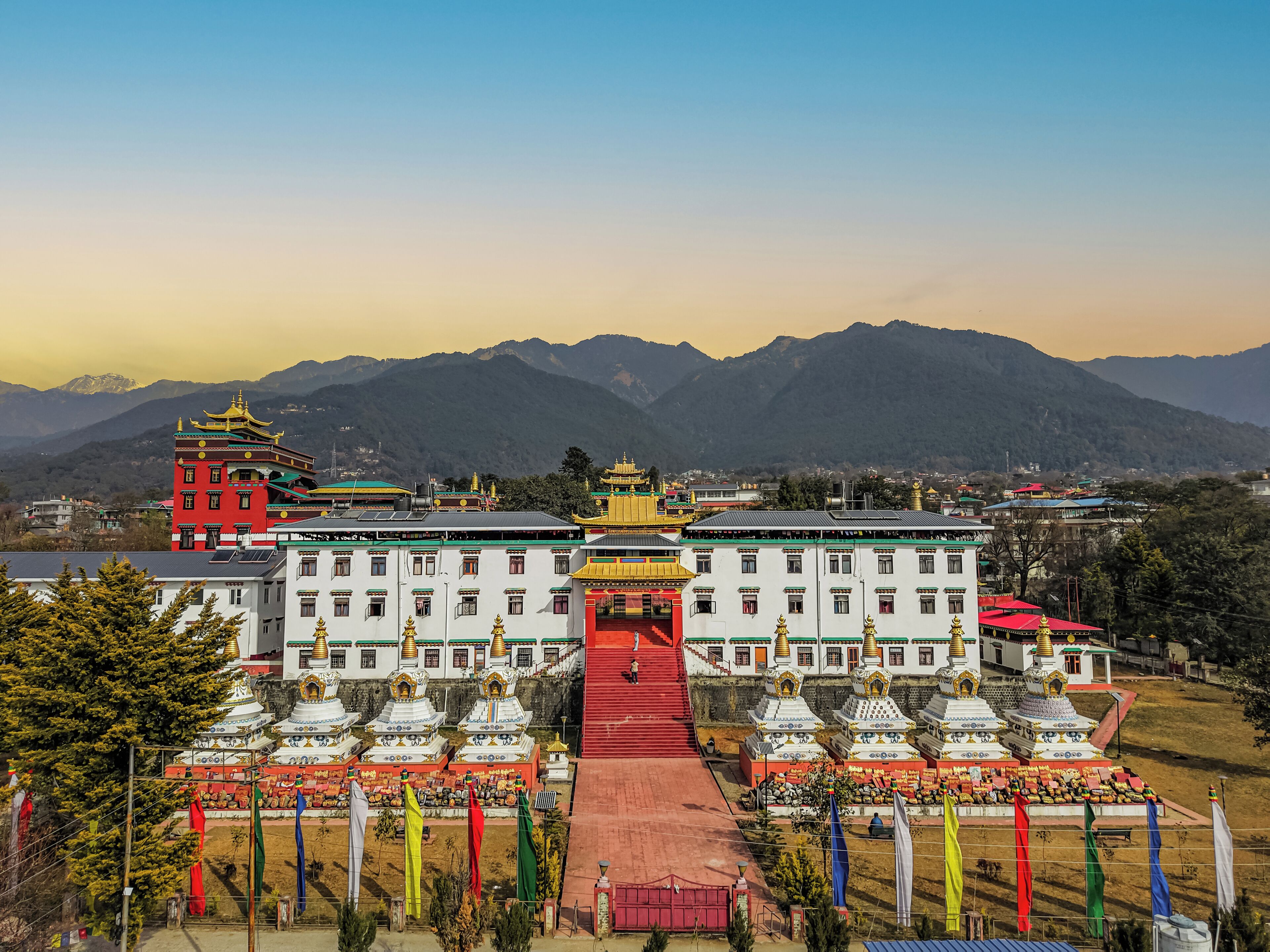 A large building with multiple white and red structures, surrounded by mountains and flags.