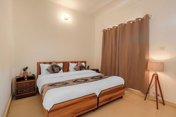 A neatly made bed with a wooden frame, a bedside table with drawers, a lamp, and a curtain.