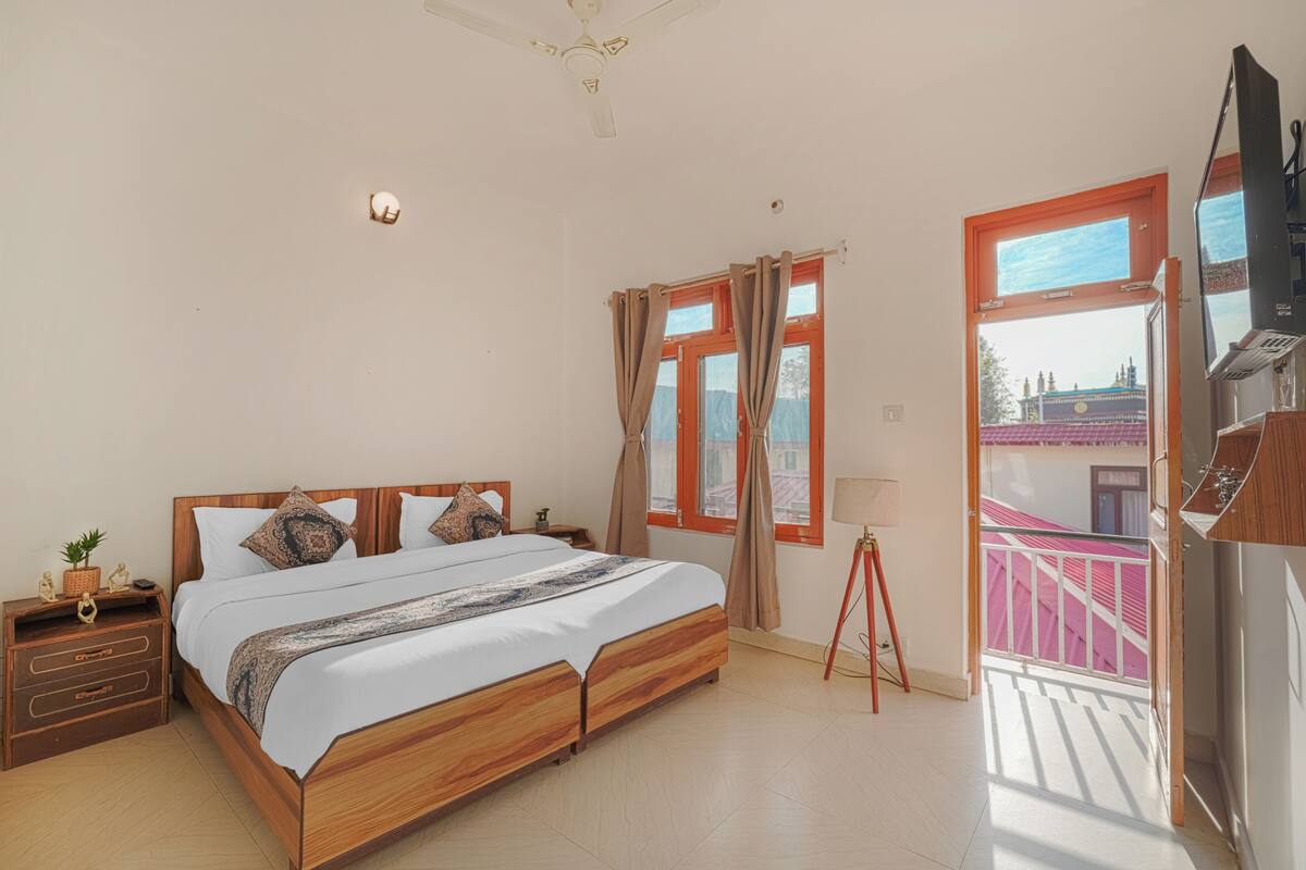 A bedroom with a wooden bed, a nightstand, a lamp, and a balcony with a view of buildings.