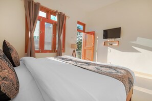 A hotel room with a large bed, a TV mounted on the wall, and a balcony with a view of the outdoors. - Bir Downtown (Baijnath)