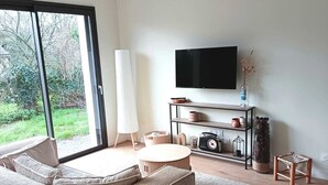 Un salon moderne avec un grand canapé, une table basse, un téléviseur et une vue sur la verdure à l’extérieur.