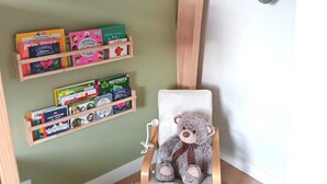 Une chambre d’angle avec une chaise en bois, un ours en peluche et une bibliothèque remplie de livres pour enfants.