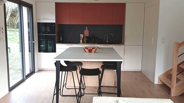 Une cuisine moderne avec un îlot central, des tabourets de bar noirs et une table à manger.