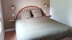 Une chambre avec un plafond en pente, un lit doté d’une tête de lit en bois, deux tables de chevet avec des lampes et une fenêtre laissant entrer la lumière naturelle.