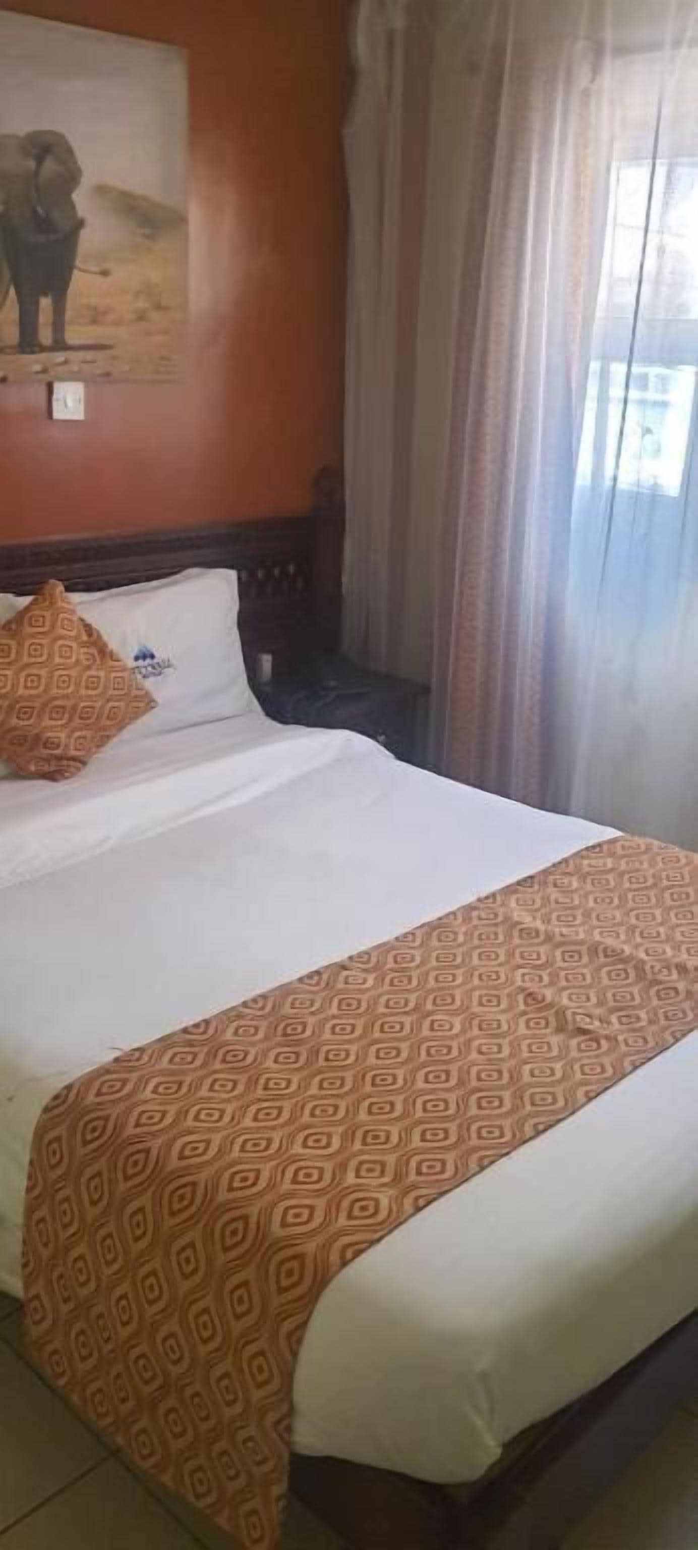Une chambre d’hôtel avec un lit, une tête de lit, une table de chevet, un tableau au mur et une fenêtre avec des rideaux.