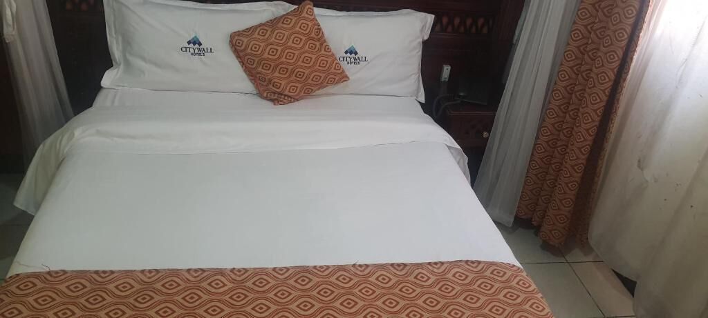 A hotel room with a bed, a patterned throw blanket, and a pillow with a geometric design.