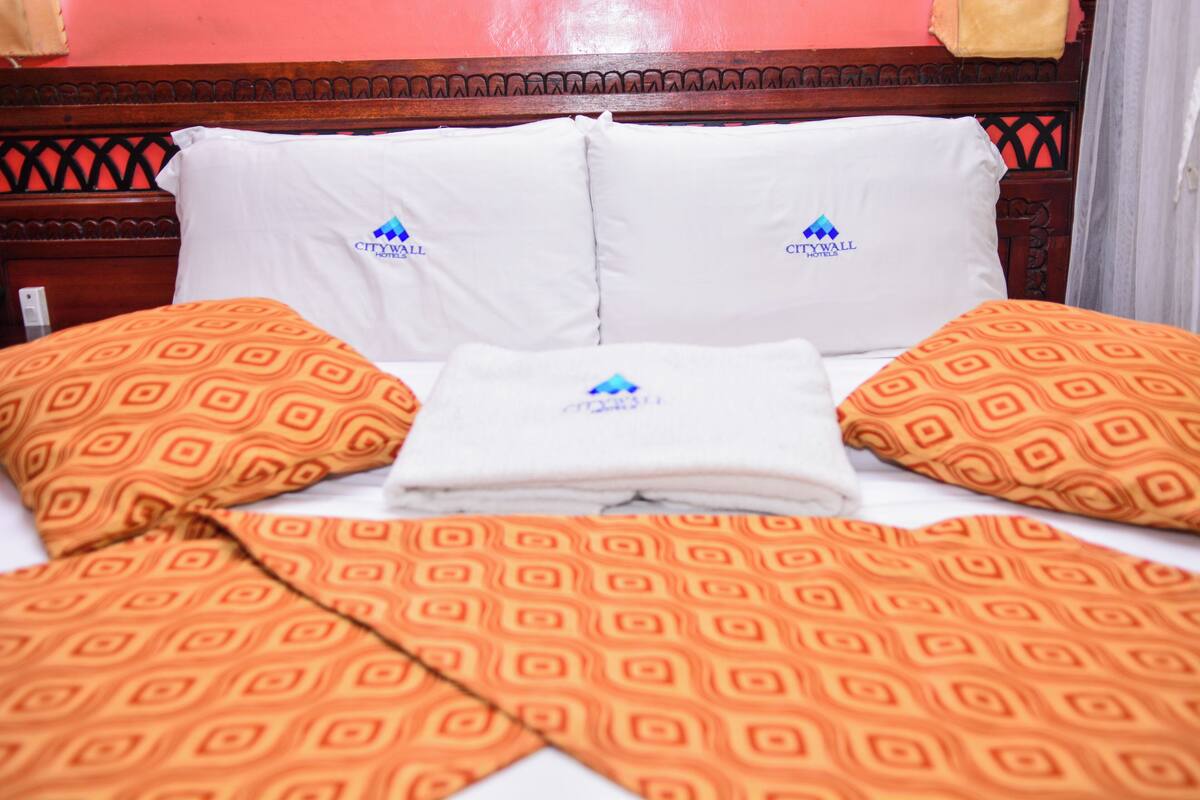 Una habitación de hotel con una cama, almohadas y una manta.