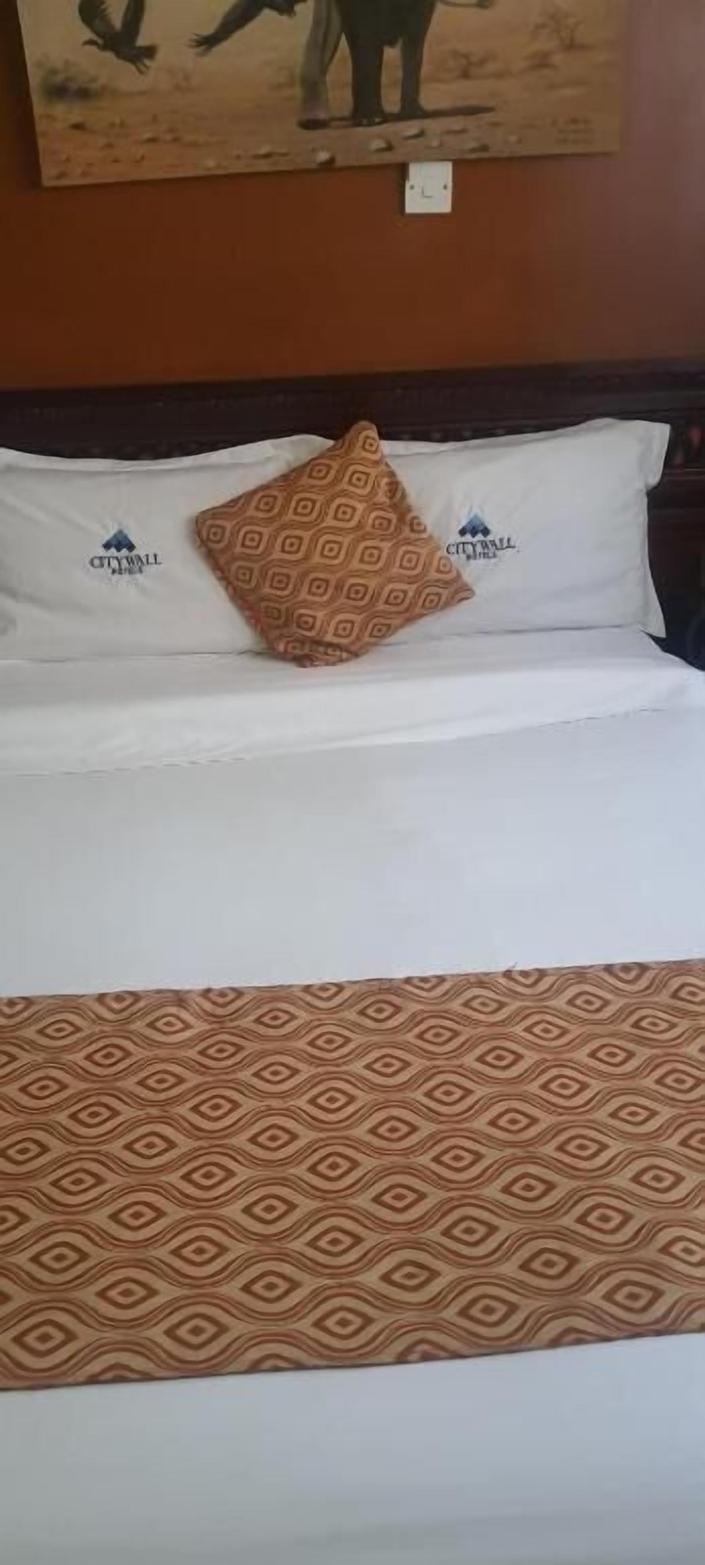 Una cama con una colcha estampada, dos almohadas con un logo y un cuadro colgado en la pared.