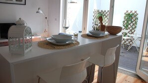 Un coin repas avec une table blanche dressée pour deux personnes, une lanterne blanche et une vue sur l’extérieur grâce à de grandes fenêtres.
