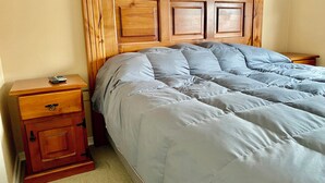 A bedroom with a wooden headboard, a bed with grey bedding, a nightstand with a remote control, and a wooden cabinet with a drawer. - Curico FULL furnished house, central location, roofed parking lot (Curicó)