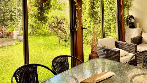 A covered patio with a glass table, wicker furniture, hanging planters, and a view of a lush garden. - Curico FULL furnished house, central location, roofed parking lot (Curicó)