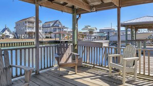 A wooden deck with two Adirondack chairs, a covered area, and a view of houses and water. - Canal Front Home, Boat Dock, Sleeps 17, Dog Friendly (Surf City)