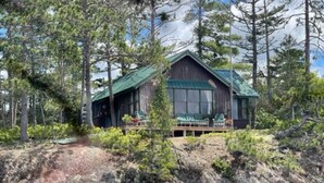 Une cabane surmontée d’un toit végétalisé, entourée d’arbres et bordée par un plan d’eau.