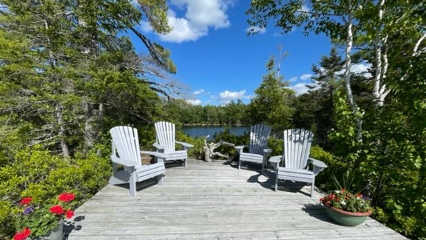 Une terrasse en bois avec des chaises Adirondack blanches et une vue sur un lac.