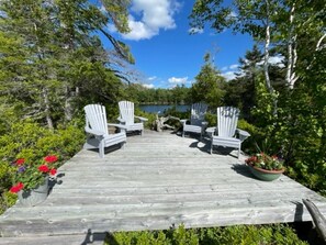 Eine Holzterrasse mit weißen Adirondack-Stühlen und Blick auf einen See.