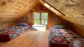 Une petite chambre mansardée avec deux lits, un plancher en bois et une fenêtre.