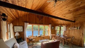L’intérieur d’un chalet chaleureux, avec des murs en bois, un canapé, un fauteuil rouge, une table à manger et une vue sur l’extérieur.