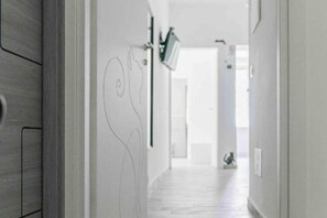 A hallway with a light-colored floor, a door at the end, and a wall-mounted light fixture. - House in the center of Amalfi enveloped by the scent of lemons, far from the chaos (Amalfi)