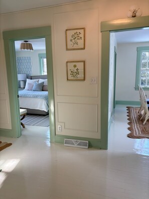 A room with a bed, a framed botanical print on the wall, and a window with a view.