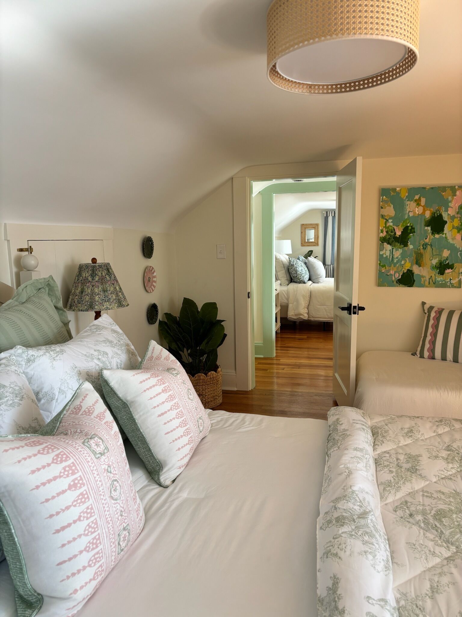 A bedroom with a large bed, multiple pillows, a hanging lamp, and a door leading to another room.