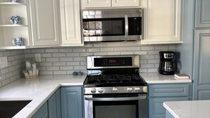 A kitchen with white cabinets, a stainless steel stove, a microwave, and a coffee maker.