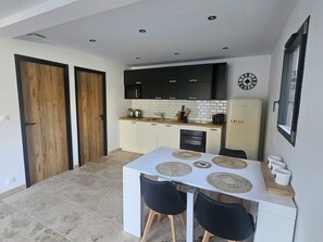 A compact kitchen with dark cabinets, a white countertop, and a dining area with a white table and two chairs. - Cosy apartment, close to beaches. Sainte Lucie de Porto Vecchio (Sainte lucie de porto vecchio)