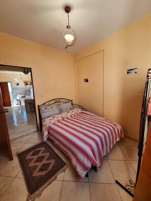 Une chambre avec un lit, un tapis, un luminaire au plafond et une vue sur la cuisine.