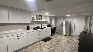 A modern kitchen with white cabinets, a stainless steel refrigerator, and a black countertop. - Elvis, Blues & BBQ: 4BR Home Just Outside Memphis, Minutes from USA Ball Stadium (Millington)